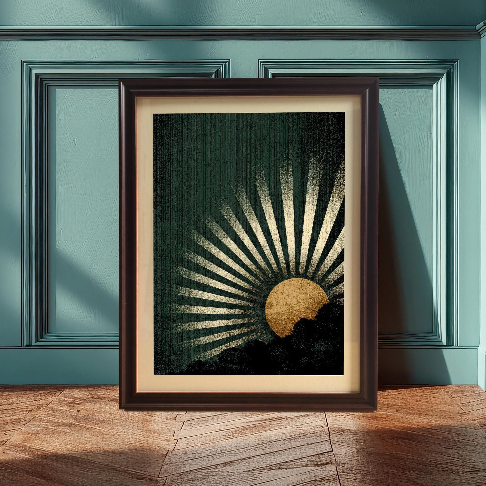 The dark green and gold sunburst art print in a Coffee Frame with a mount, leaning against a paneled teal or blue-green wall, with a wooden floor. Sunlight casts strong shadows across the floor.