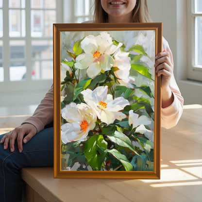 A close-up shot of a person holding an original oil painting of vibrant white flowers with thick impasto brushstrokes. The painting is in a gold-colored wood frame. The background shows a sunny, brightly lit room with large windows.