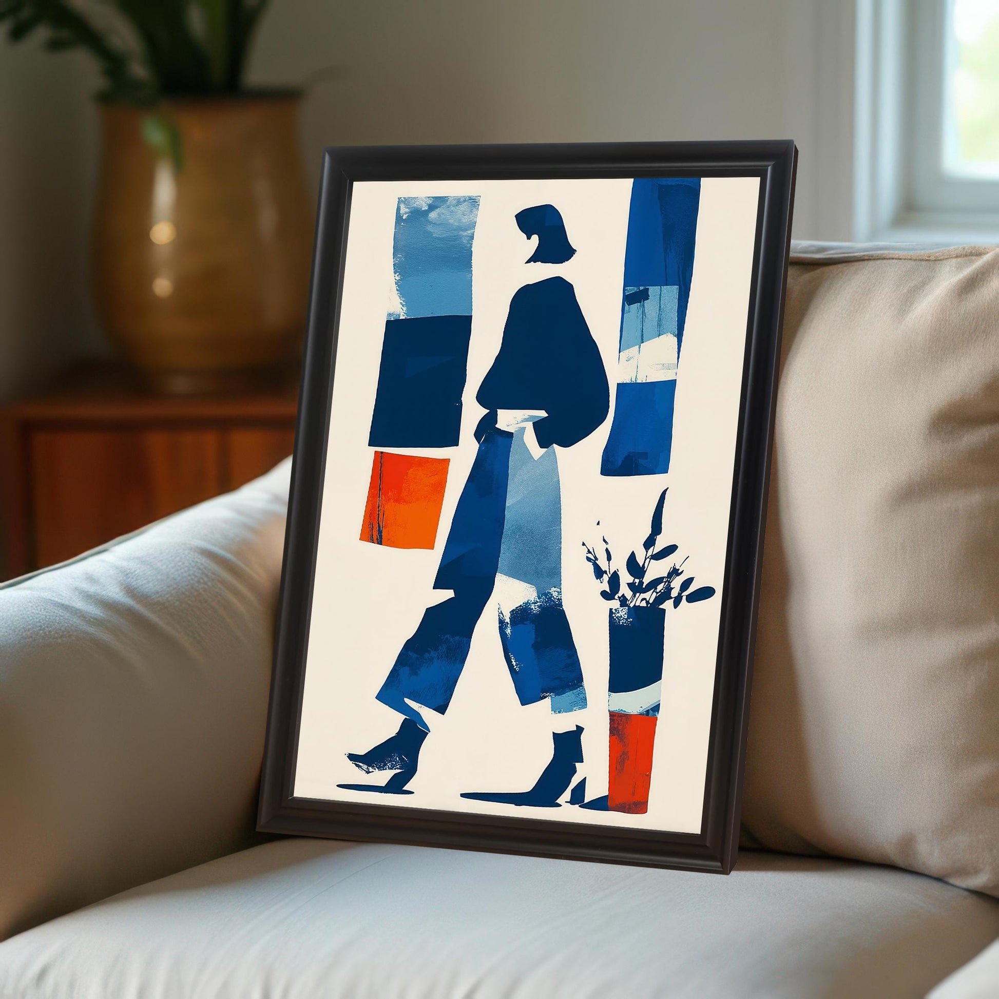 Close-up shot of the abstract print in a dark brown/black frame resting on the arm or cushion of a cream-colored upholstered sofa.