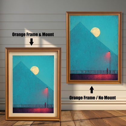 Comparison image showing two framed art prints against a white wainscoting wall. The left print uses an Orange Frame & Mount (matting). The right print uses an Orange Frame / No Mount. The art depicts a minimal landscape with a figure, a red lamp post, and a pyramid under a moon.