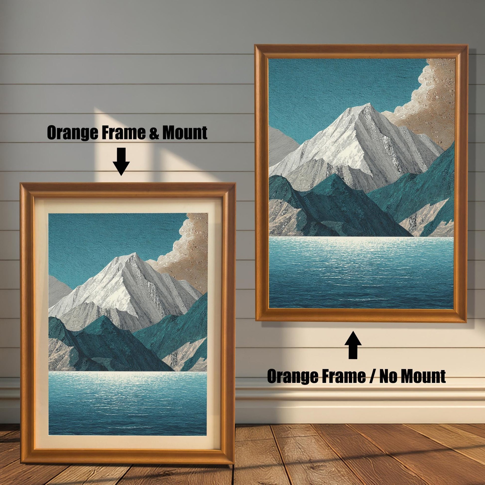 A comparison image showing two framed art prints on a wooden wall. The print on the left is in an Orange Frame & Mount (golden/orange frame with a light mat). The print on the right is in an Orange Frame / No Mount (golden/orange frame, no mat). Both feature the mountain and lake design.