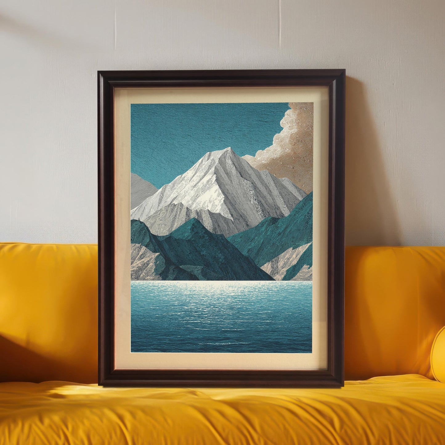 The mountain and lake art print in a dark brown/coffee frame with a mount/mat, positioned centrally on a bright, vibrant yellow sofa or cushion.