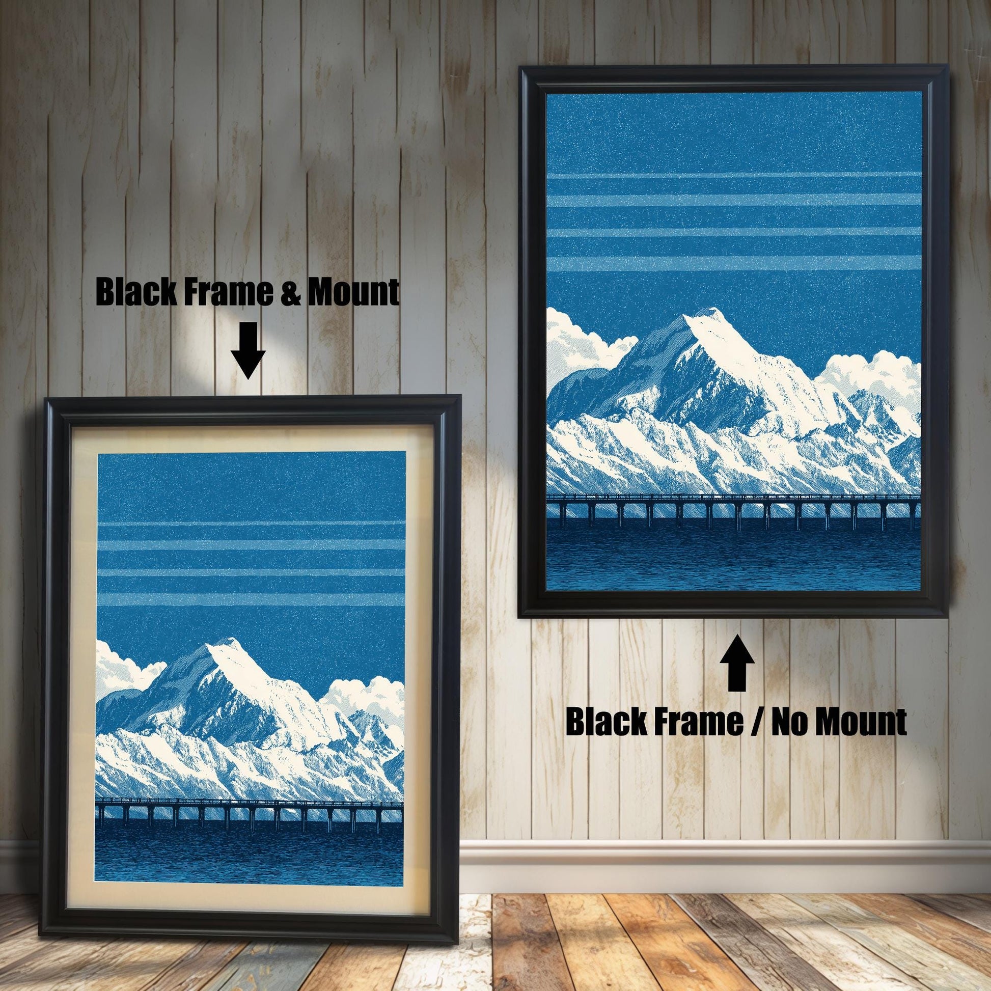 A comparison image showing two framed art prints on a wooden wall. The print on the left is in a Black Frame & Mount (black frame with a light mat). The print on the right is in a Black Frame / No Mount (black frame, no mat). Both feature the blue mountain and bridge design.