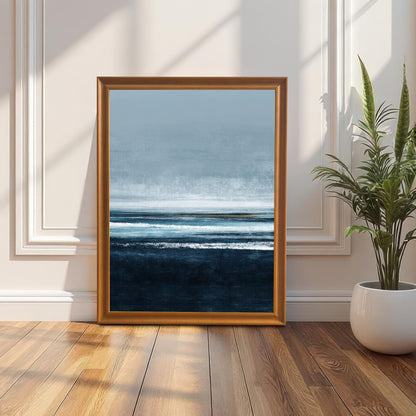 Abstract seascape art print in an Orange/light brown wood frame (no mount), leaning on a sunlit wooden floor against a white paneled wall. A tall snake plant in a white pot is on the right. Ideal for coastal or modern decor.