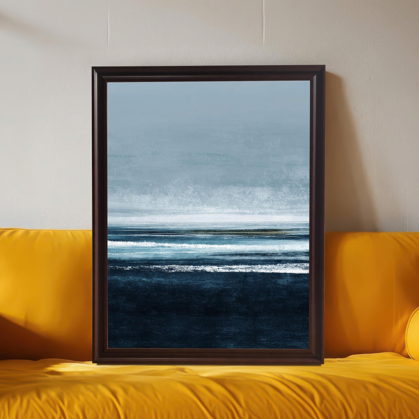Large abstract seascape framed art print, displayed in a Coffee (dark brown) frame leaning on a bright yellow sofa. The art features dark blue water and a pale blue horizon. Shows the print used as a statement piece in colorful decor.