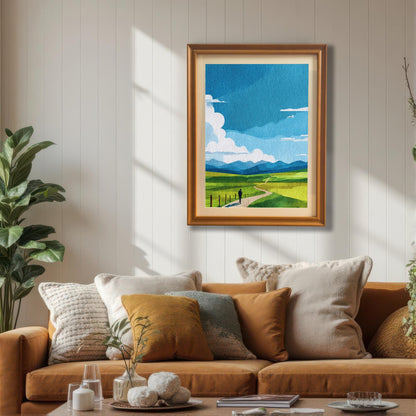 Abstract landscape print featuring rolling green hills, a winding path with a lone figure, and a bright blue sky with white clouds. The print is displayed in an Orange/light brown wood frame hanging above a tan sofa with pillows, in a sunlit living room with a houseplant.