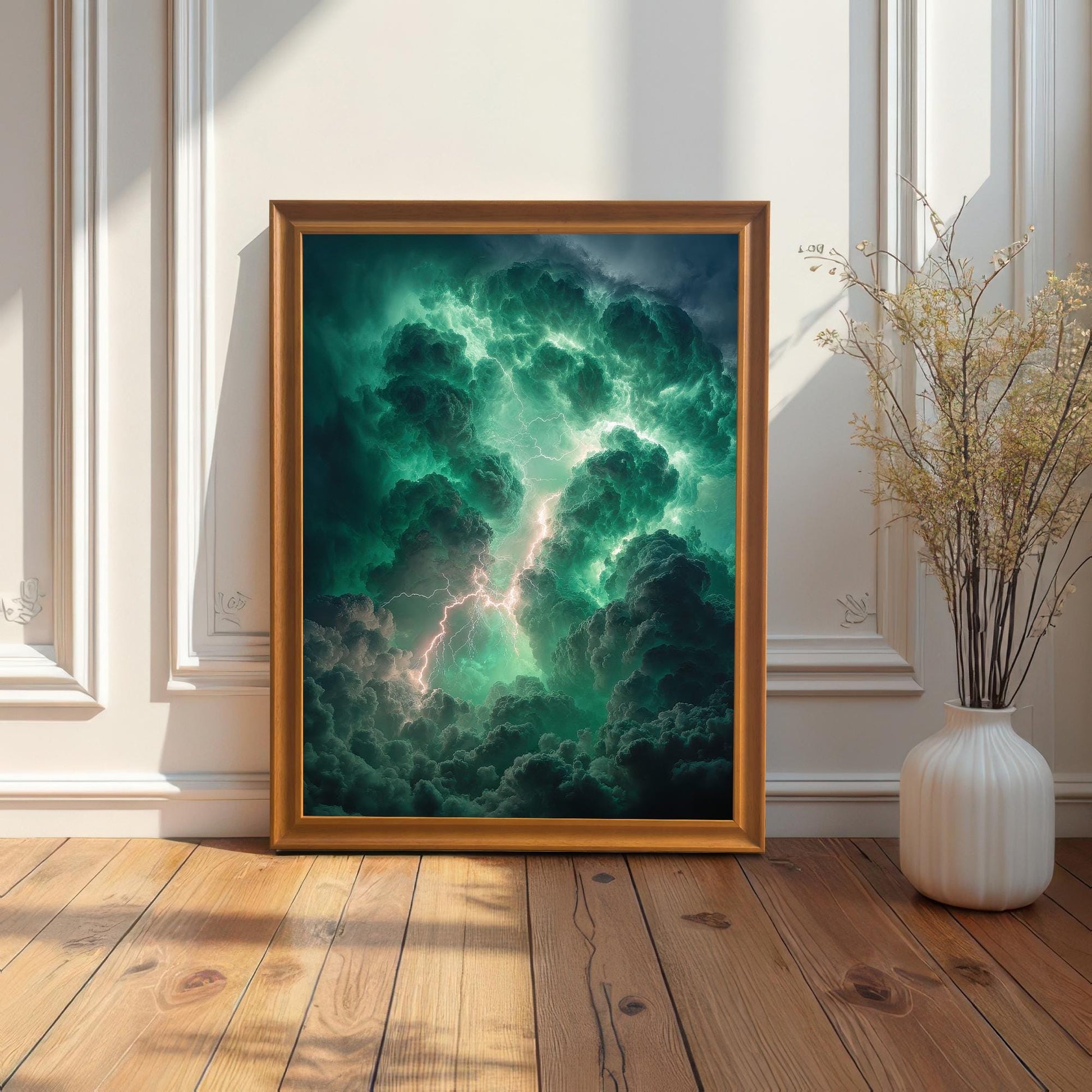 A framed art print of dramatic green and dark storm clouds with lightning resting on a wooden floor, leaning against a white wainscoted wall, next to a white vase with dried reeds. The frame is Orange (light brown wood color).