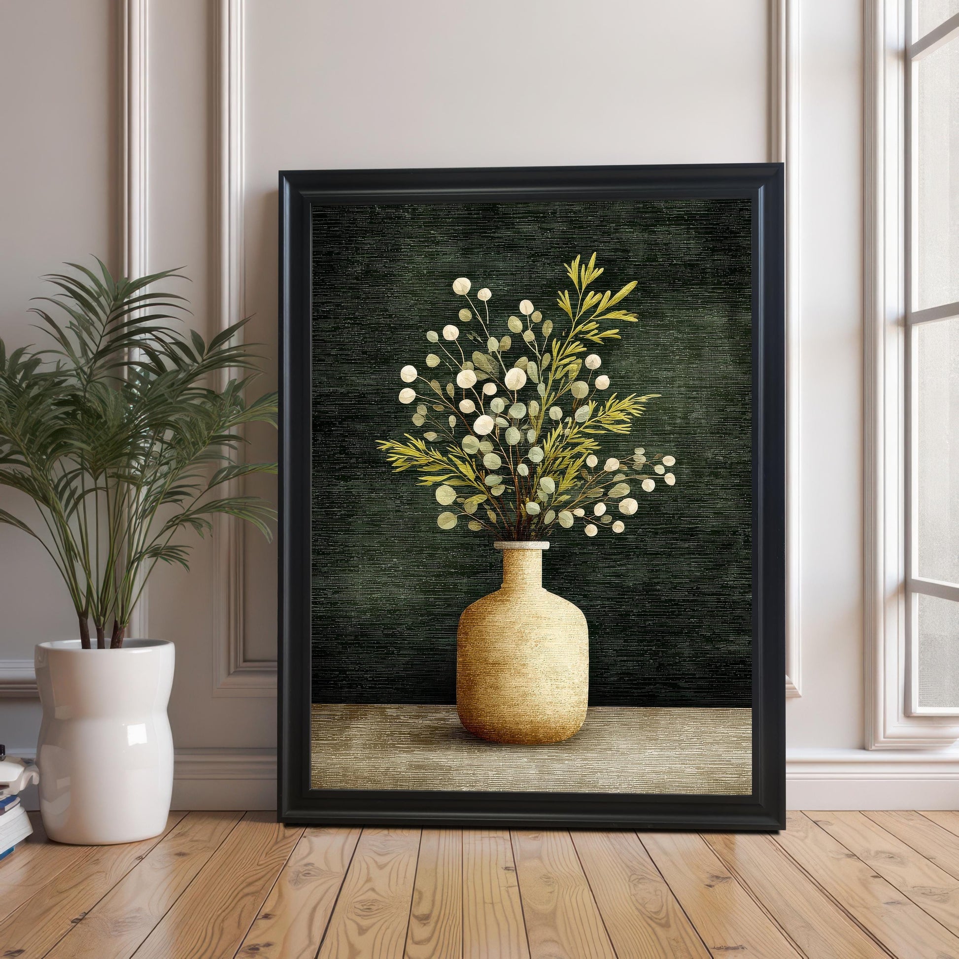 A large framed art print of a vase with foliage, resting on a wooden floor against a wall with white molding. The frame is Black with no mount/border visible. A potted green plant is visible on the left.
