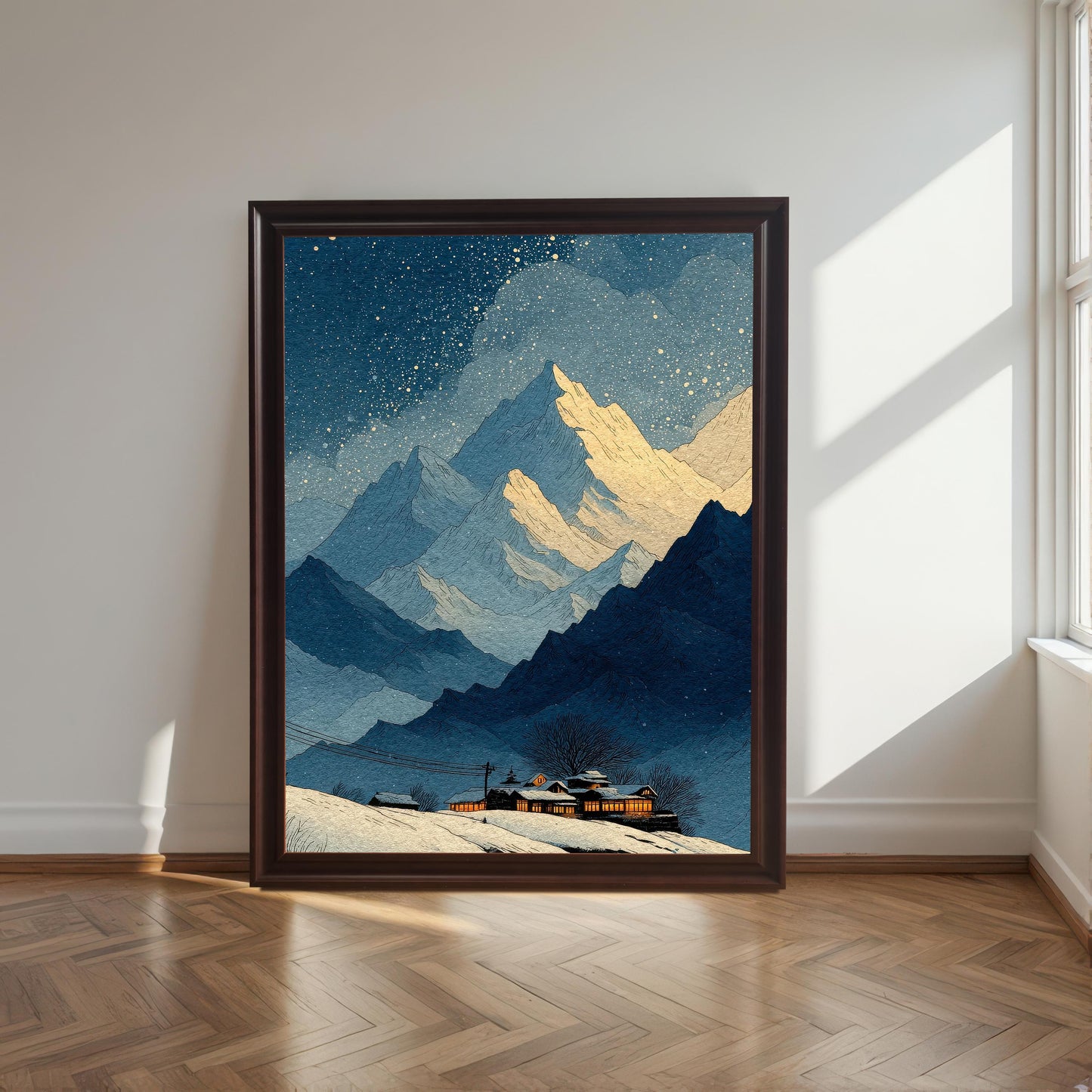A large framed art print of the snowy mountain landscape (featuring blue mountains, golden peaks, and a lit cabin), resting on a herringbone wood floor against a white wall near a sunlit window. The frame is a dark brown (Coffee) wood.