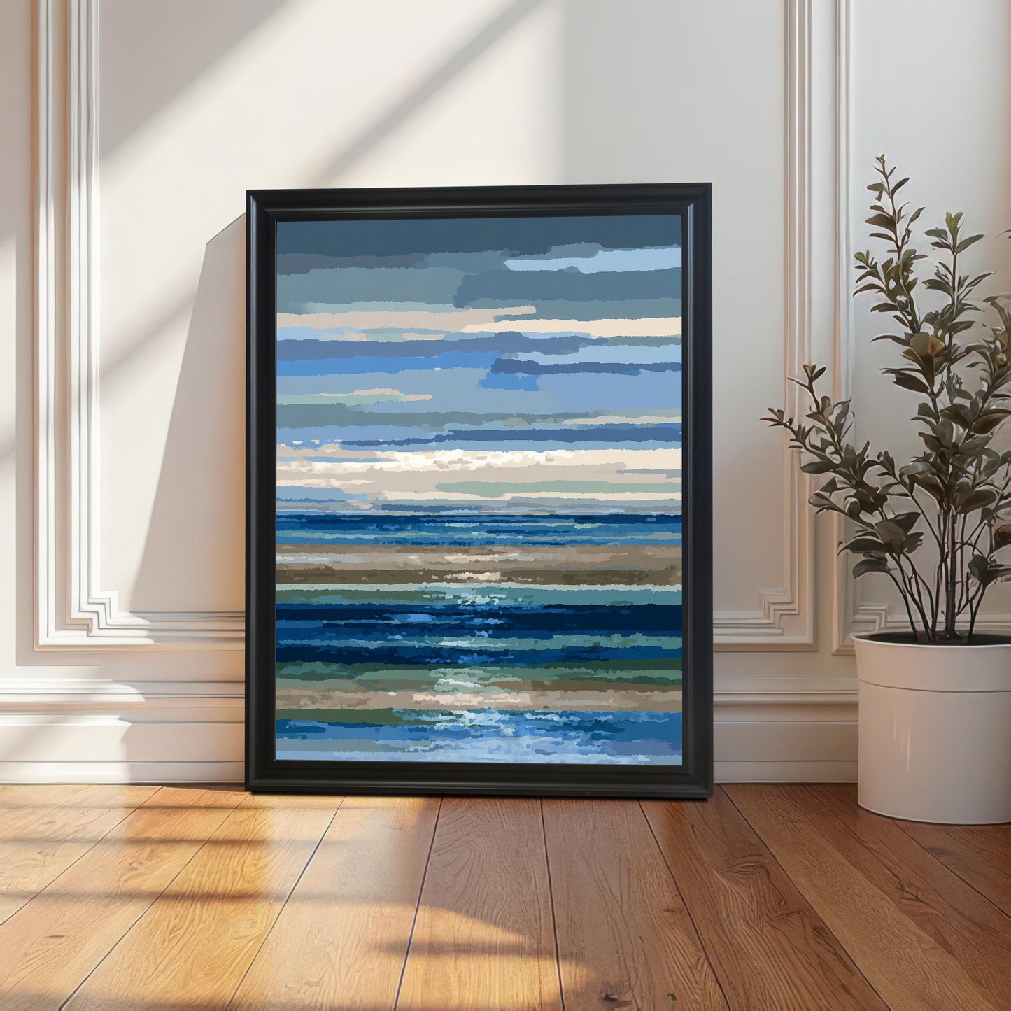 Abstract blue and brown striped seascape art print in a simple black frame, leaning on a wooden floor against a white paneled wall next to a potted plant, with long shadows from sunlight.