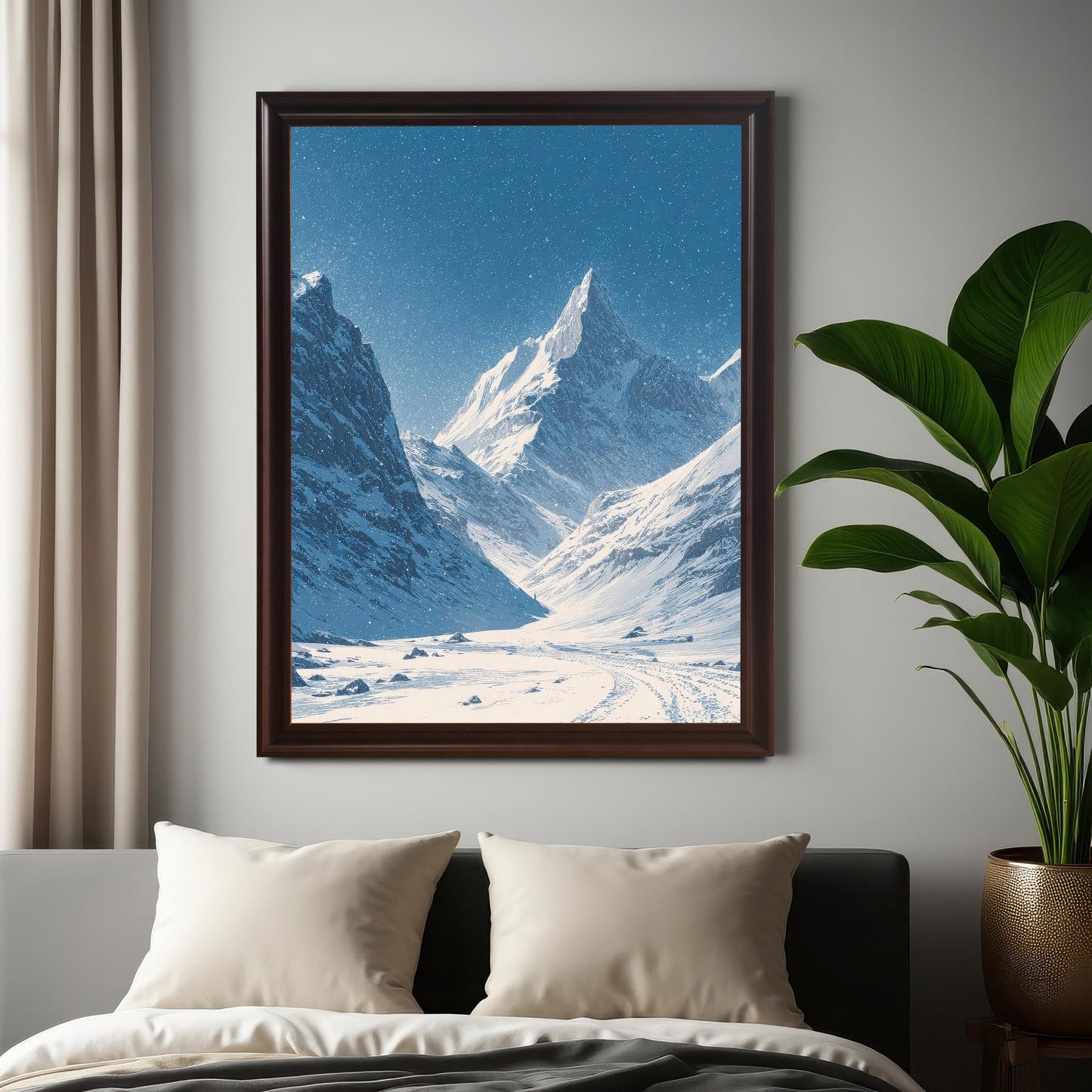 Large snowy mountain valley print in a dark brown frame, hanging on a gray wall above a bed with pillows, next to a large potted green plant.
