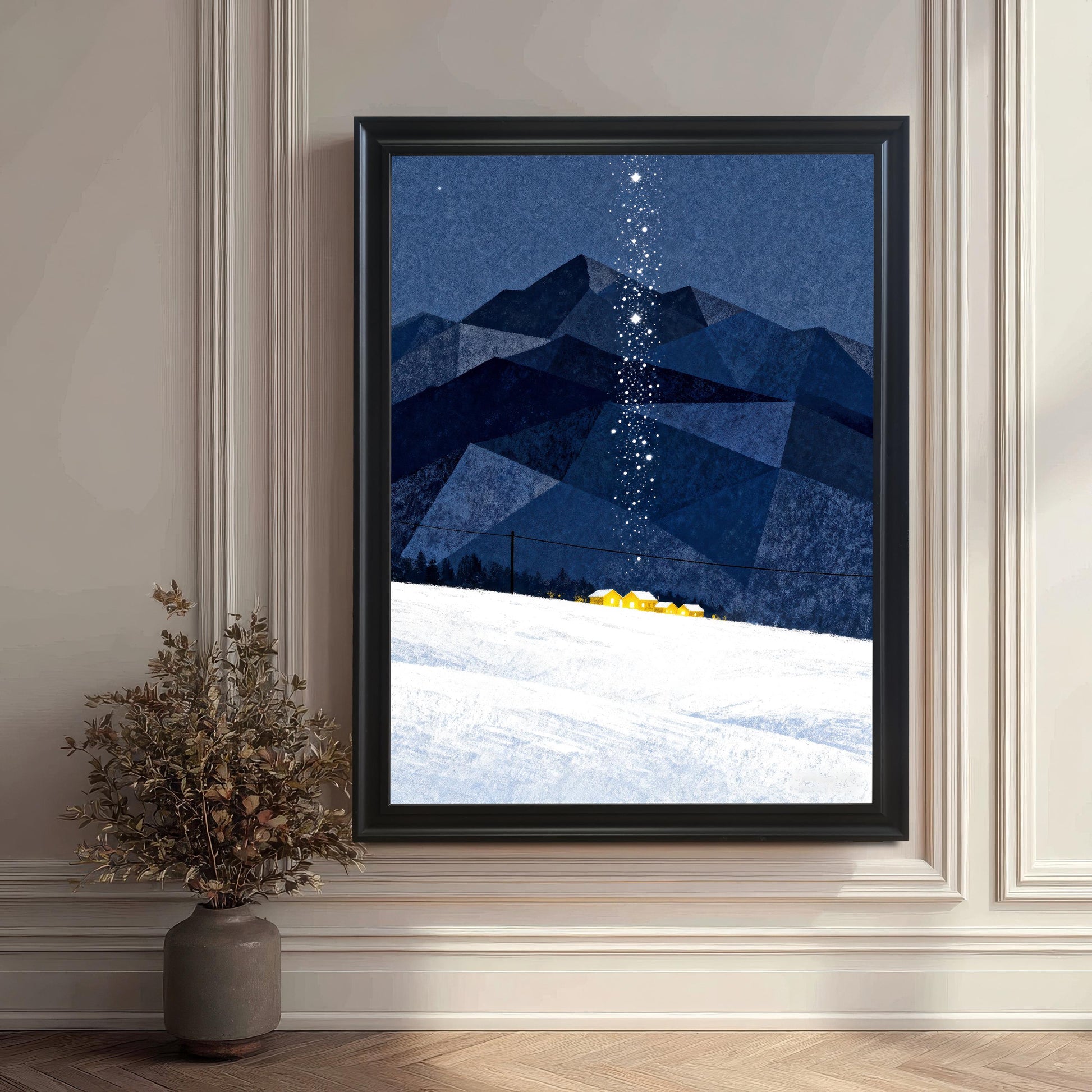 Large framed art print in a Black Frame, featuring blue geometric mountains, a white snowfield with small yellow houses, and a vertical trail of stars, leaning against an ornate off-white paneled wall.