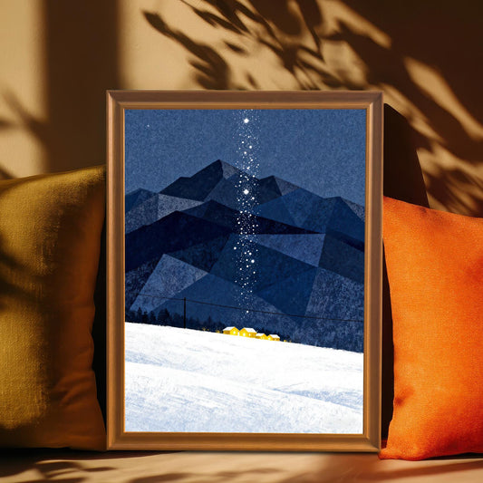 Framed art print with blue mountains and snow, set in an Orange Frame, resting between two throw pillows (one olive, one orange) with dramatic shadows across a tan wall.