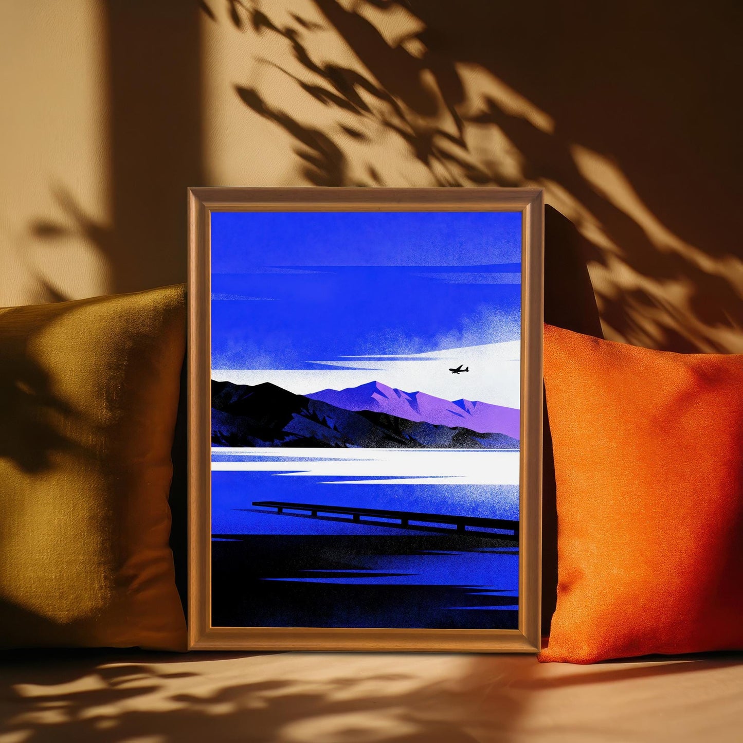 Blue Lake/Mountain	Framed Blue Lake/Mountain art print in an Orange Frame, resting between two throw pillows (one olive, one orange) with dramatic shadows across a tan wall.