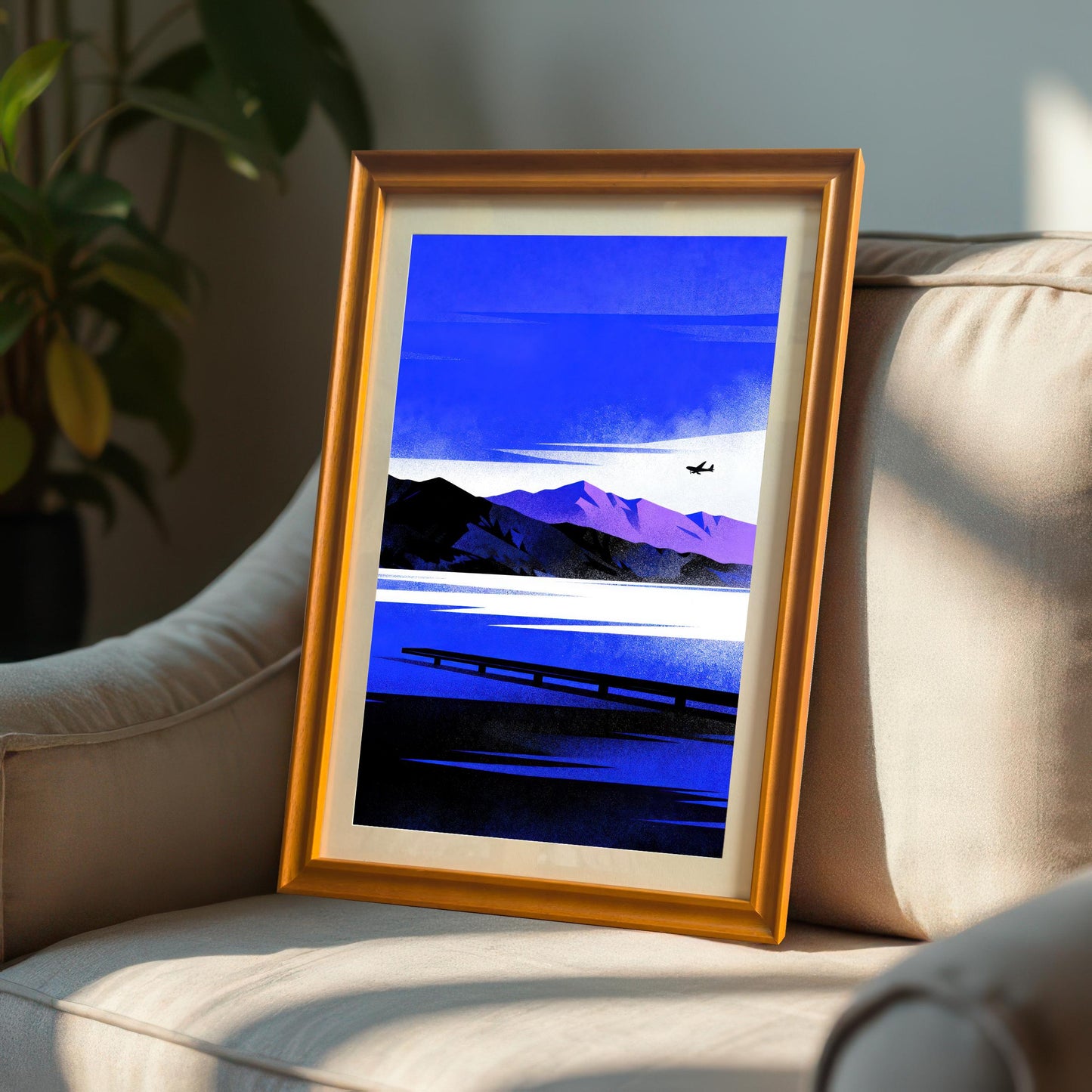 Blue Lake/Mountain	Framed Blue Lake/Mountain art print in an Orange Frame with a mount, resting on a beige armchair in sunlight next to an indoor plant.