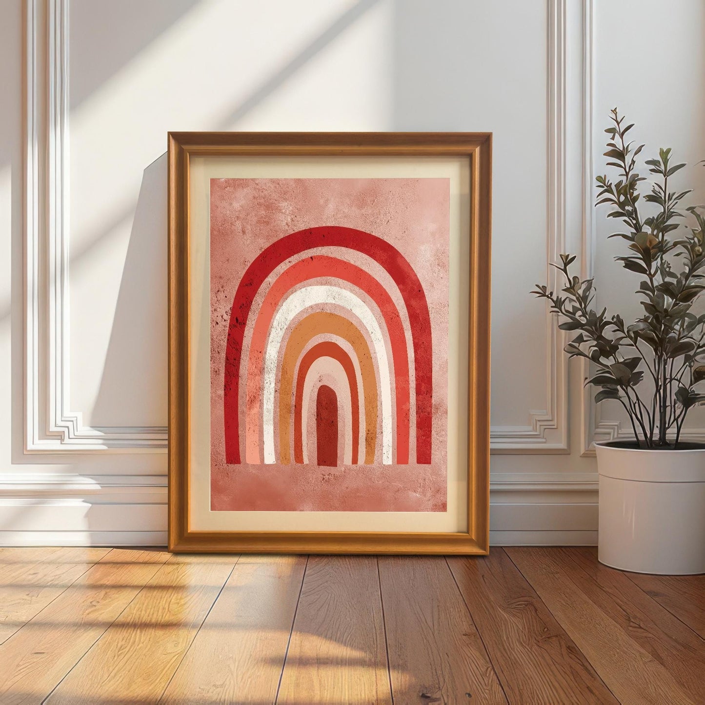 The boho rainbow art print framed in an Orange/light brown frame with a mat (mount), leaning against a white wainscoted wall next to a large potted plant. Sunlight and shadows fall on the wall and wooden floor.