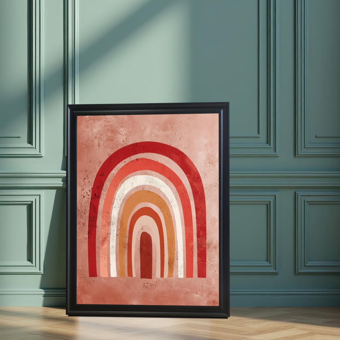 The framed boho rainbow art print in a Black frame with no mat, leaning on a wooden floor against a wainscoted wall painted in a dark sage green color. Sunlight and plant shadows fall across the art and wall.
