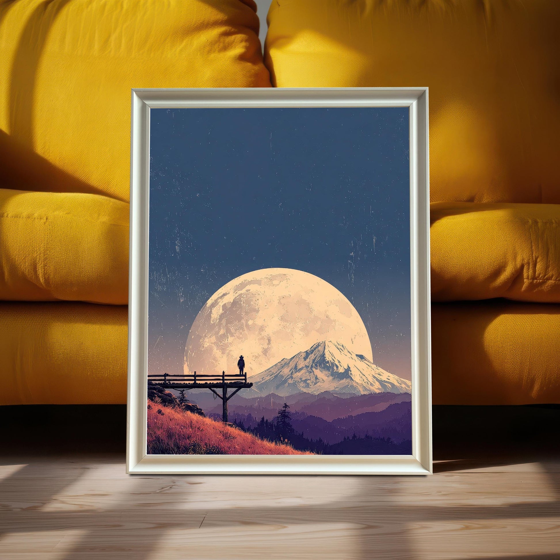 Landscape art print in a white/silver frame, featuring a large moon over a mountain, leaning on the floor against a bright yellow sofa.