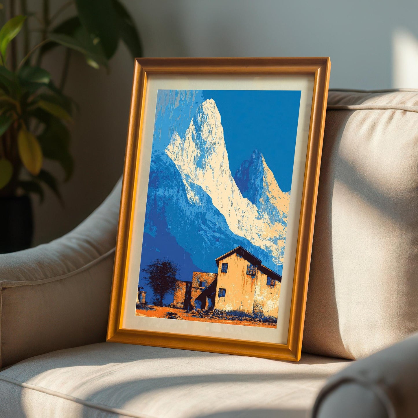 Landscape art print in an orange/light brown wood frame with a mount, propped up on a textured, neutral-colored armchair.