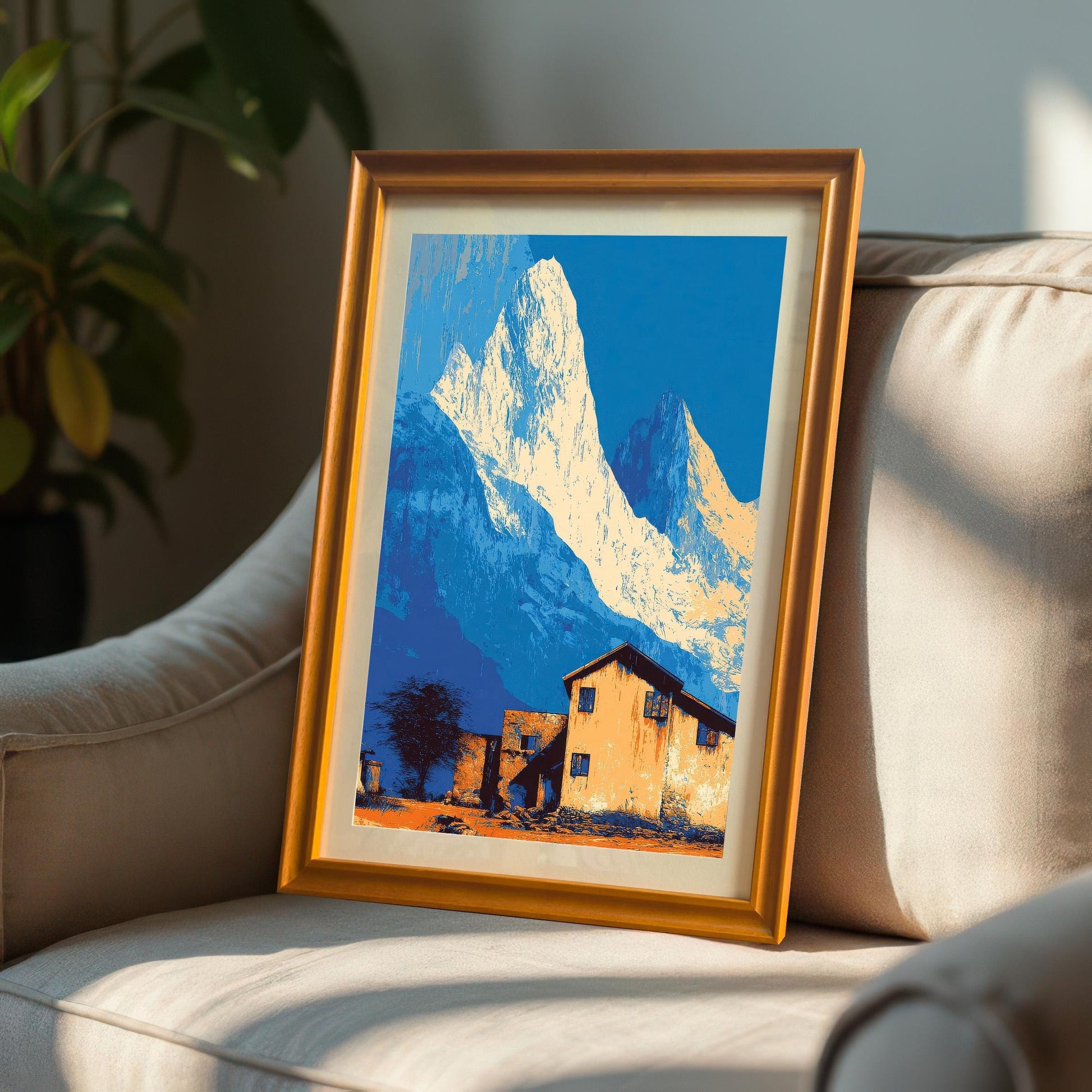 Landscape art print in an orange/light brown wood frame with a mount, propped up on a textured, neutral-colored armchair.