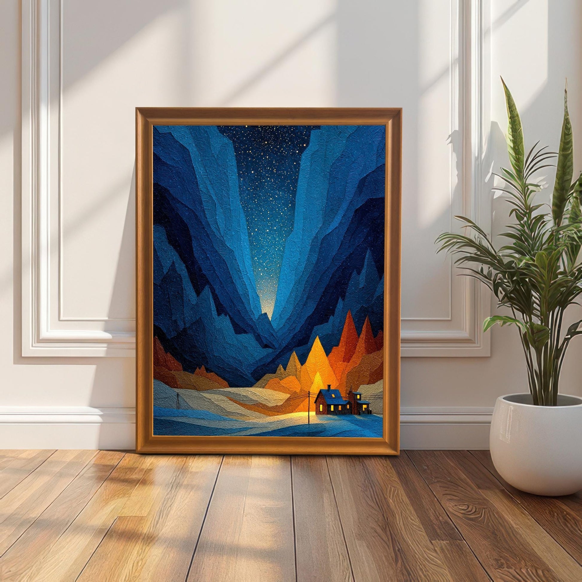 The framed art print, featuring a geometric blue mountain valley, a starry sky, and an illuminated cabin, leaning against a white wainscoted wall on a wooden floor in a sunlit room. The frame is Orange (or light wood).