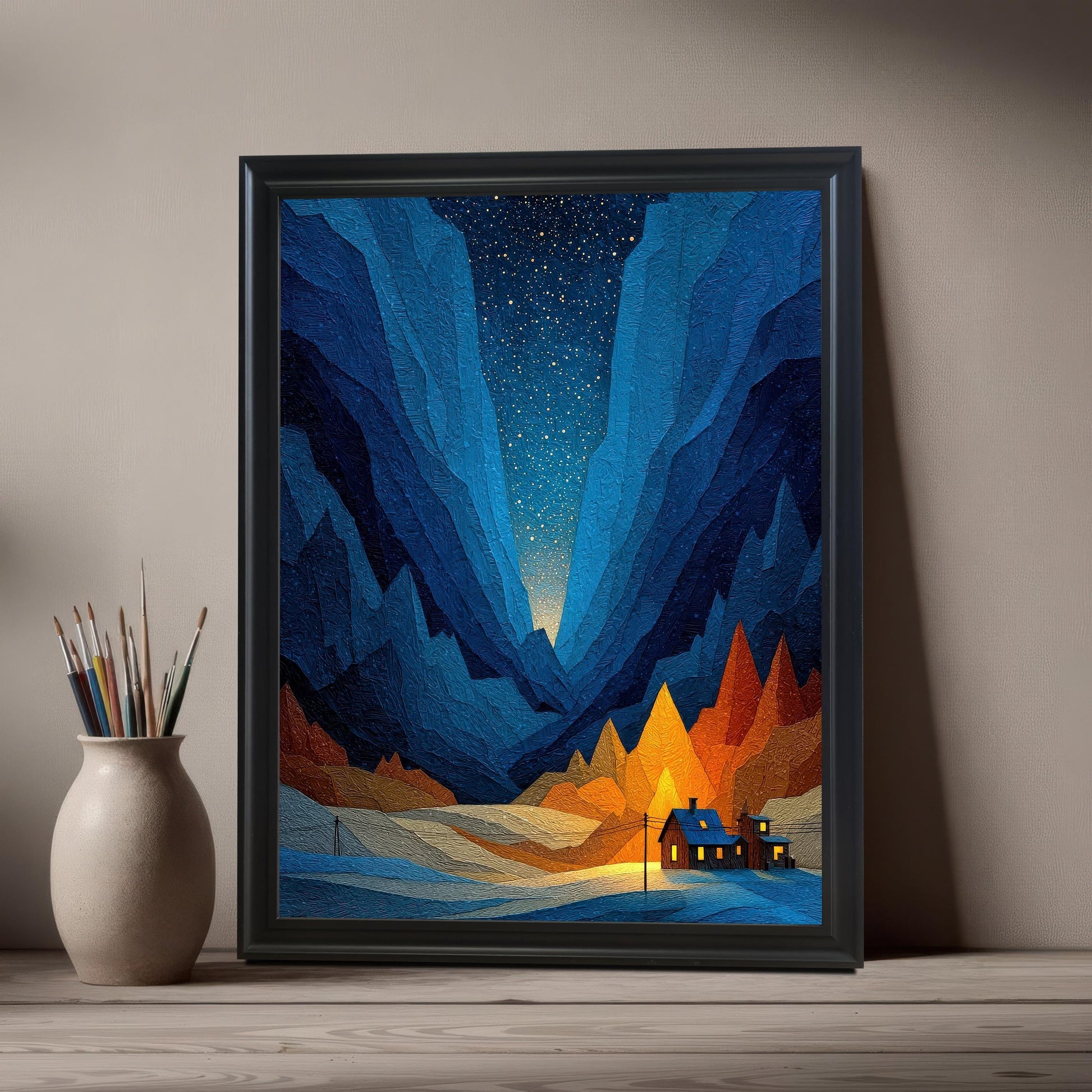 A close-up of the geometric mountain art print in a Black Frame / No Mount (full bleed print) leaning on a light wooden table next to a vase holding paintbrushes.