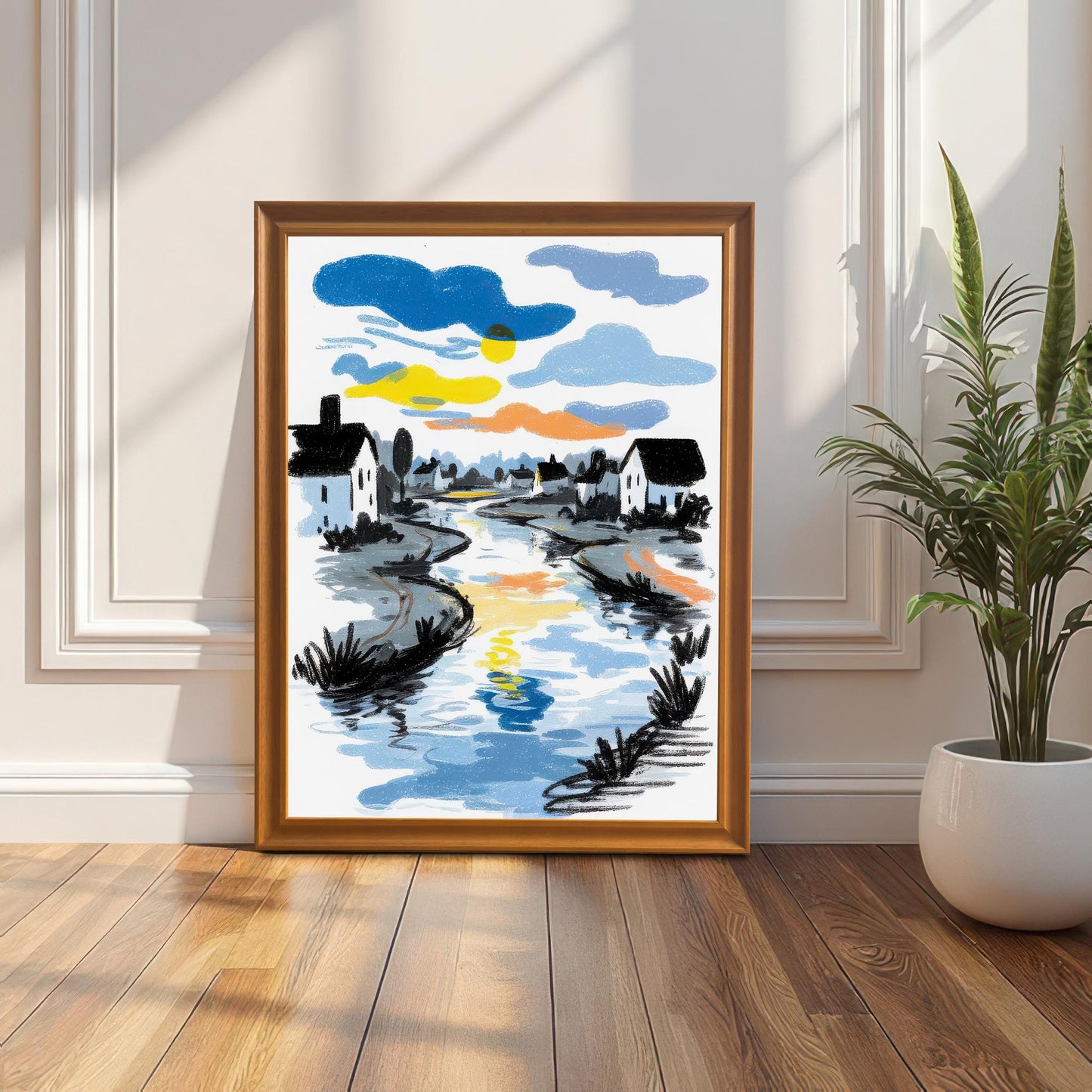 The framed sketch-style art print, featuring a river and white houses under a colorful sky, leaning against a white wainscoted wall on a wooden floor in a sunlit room. The frame is Orange (or light wood).