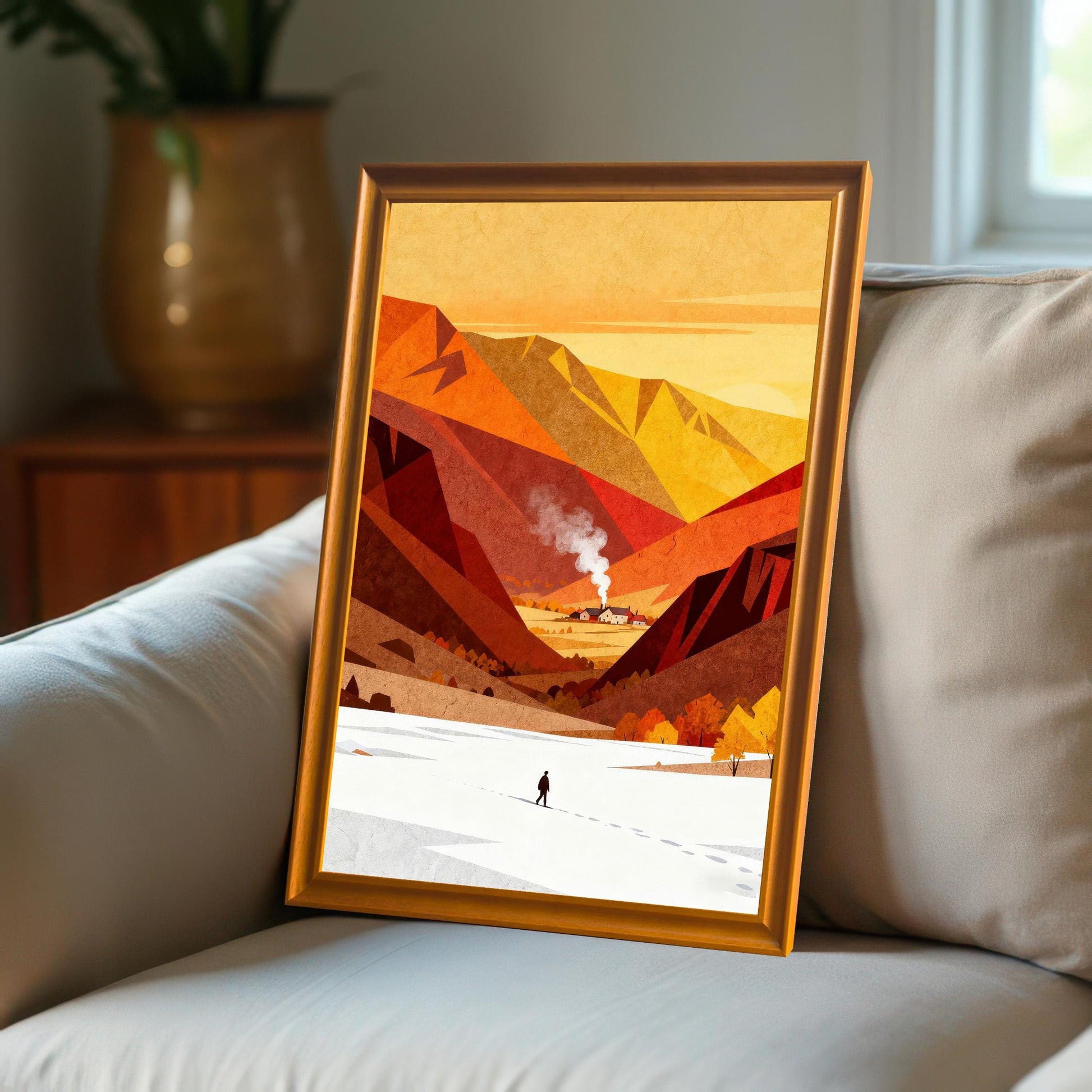 A framed orange and red mountain landscape print leaning against a soft beige sofa cushion in a cozy, modern interior setting.