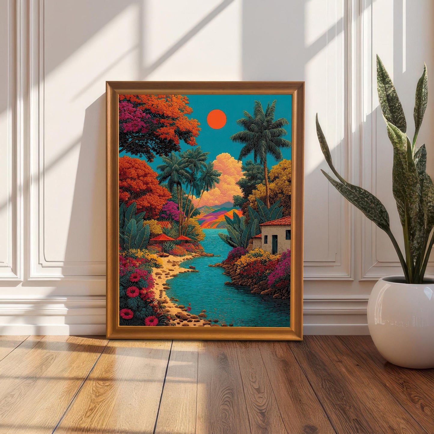 The vibrant tropical landscape art print in a gold/orange wooden frame, standing on a hardwood floor, leaning against a white wainscot wall next to a tall potted snake plant.