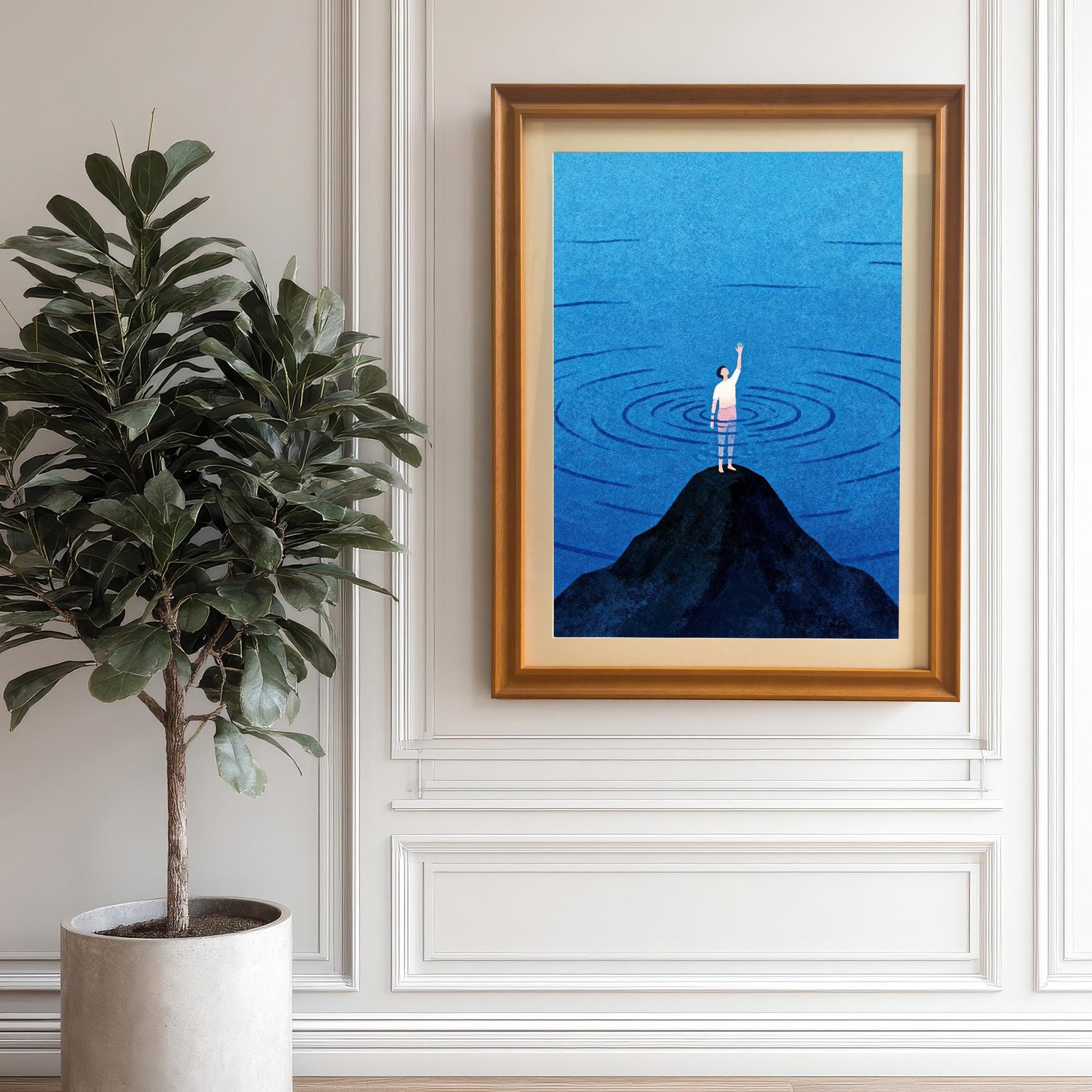 A large orange wood-framed print with a mat (mount) hanging on a classic white wainscoted wall. A large potted fiddle-leaf fig plant sits to the left, creating a clean and elegant interior decor scene.