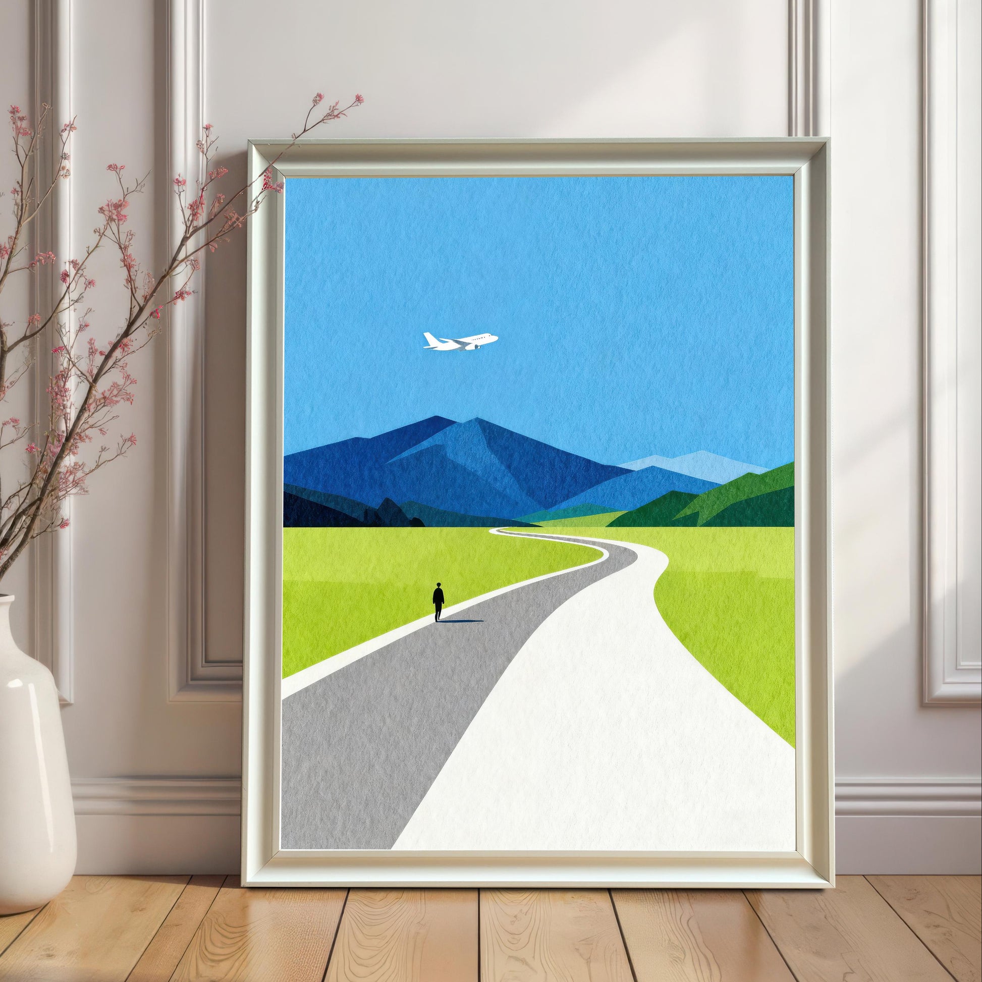A white wood framed landscape print without a mount, displayed on a light wood floor against a white paneled wall next to a minimalist ceramic vase with dried branches.