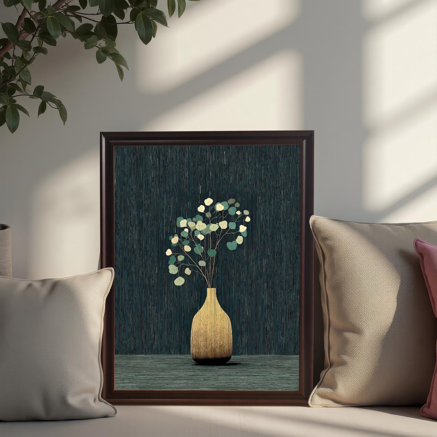 The golden vase and eucalyptus art print in a Coffee Frame with a mount, propped up on a couch surrounded by light-colored pillows, with a potted plant visible above.