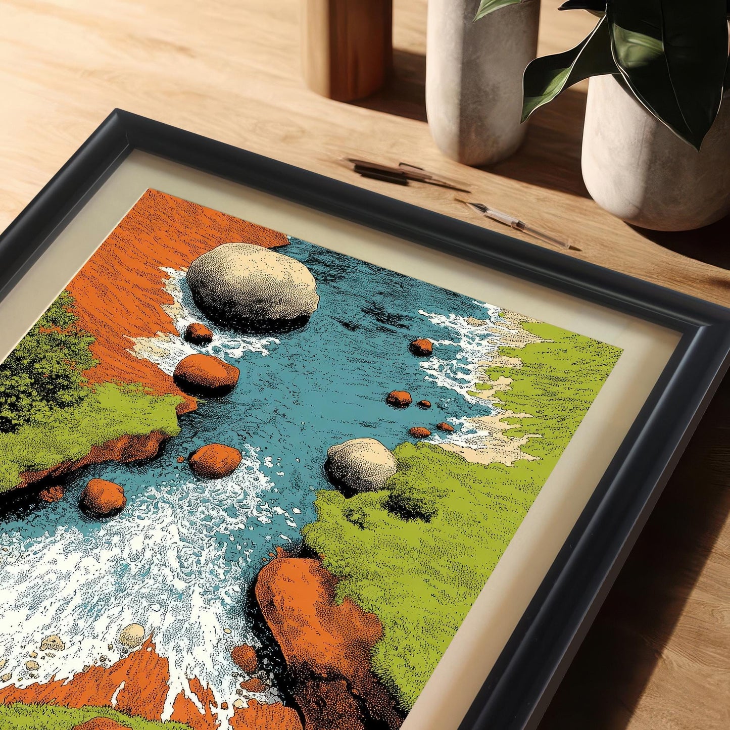 Extreme close-up shot of the framed art print (black frame with matting) lying on a wooden desk. The image highlights the texture and vibrant colors of the rocky river scene, including the blue water, white rapids, green banks, and orange rocks.