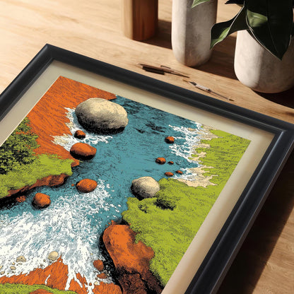 Extreme close-up shot of the framed art print (black frame with matting) lying on a wooden desk. The image highlights the texture and vibrant colors of the rocky river scene, including the blue water, white rapids, green banks, and orange rocks.