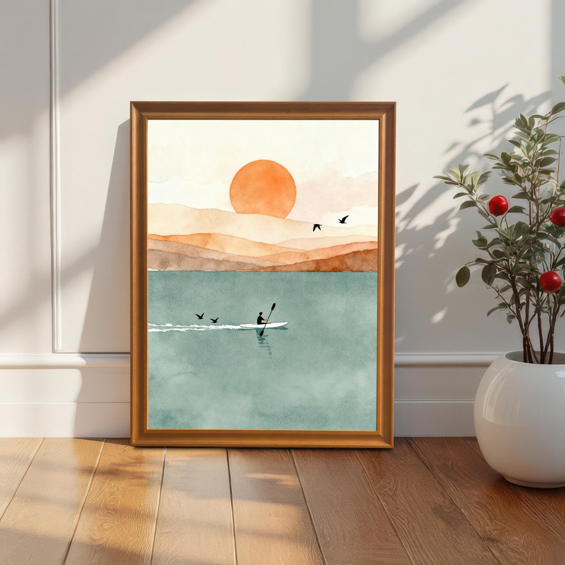 Orange wood frame without a mount featuring a kayak on a teal lake, placed on a hardwood floor next to a white potted plant.