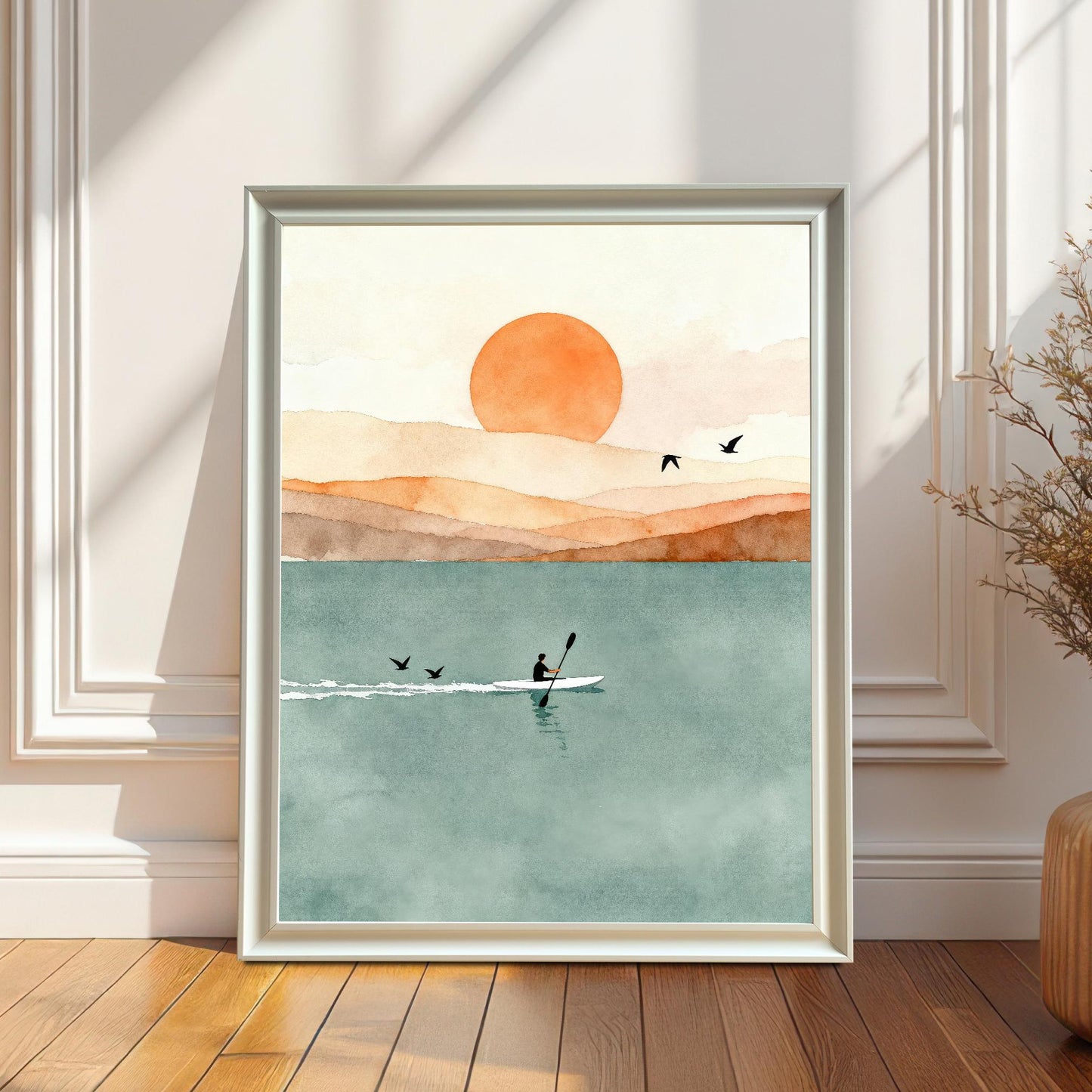 White wood frame featuring a serene watercolor of a kayaker at sunset, styled on a wood floor next to a tall vase of dried plants.