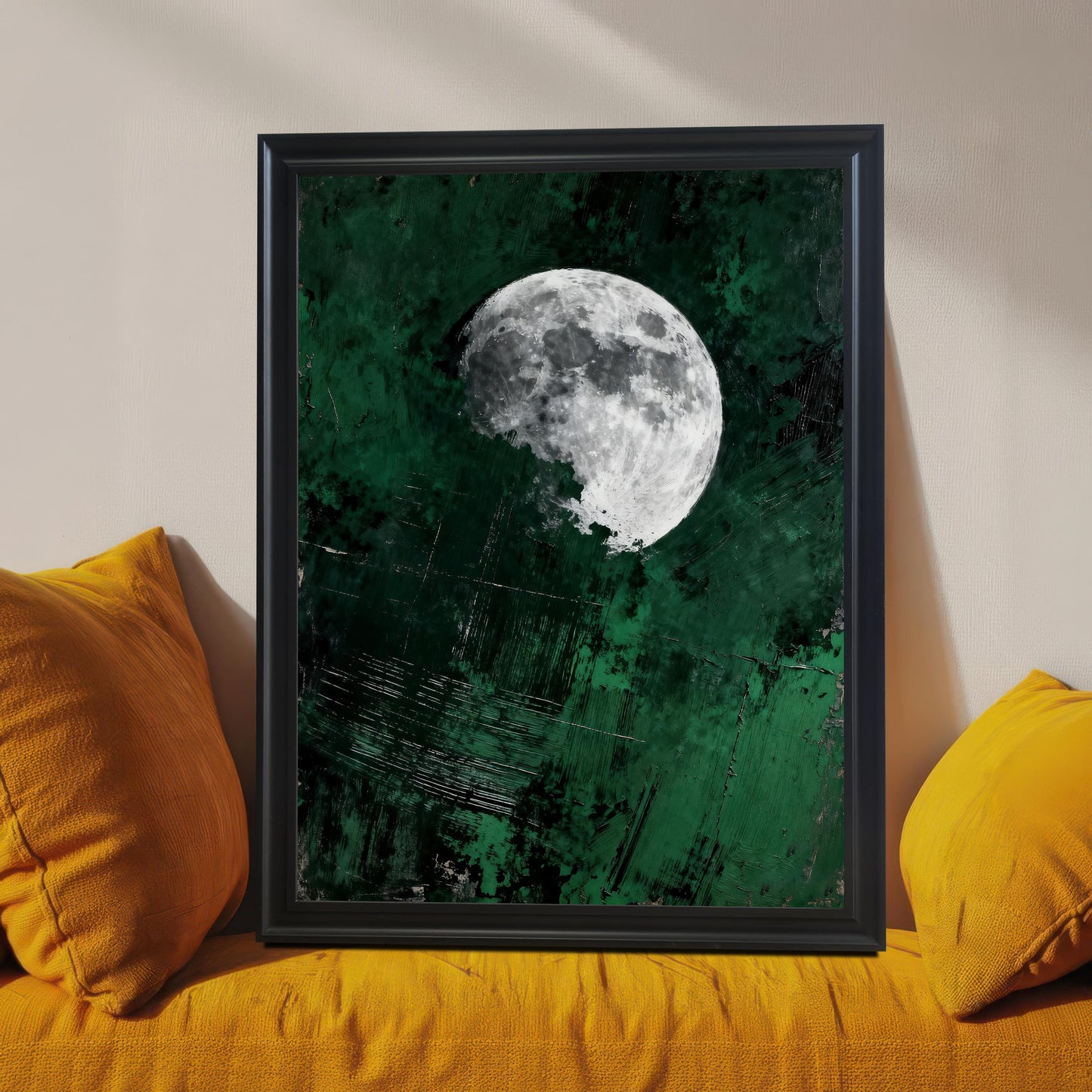 Close-up of a black wood-framed moon art print leaning on a vibrant orange textured sofa, highlighting the detail of the emerald green background and high-contrast moon.
