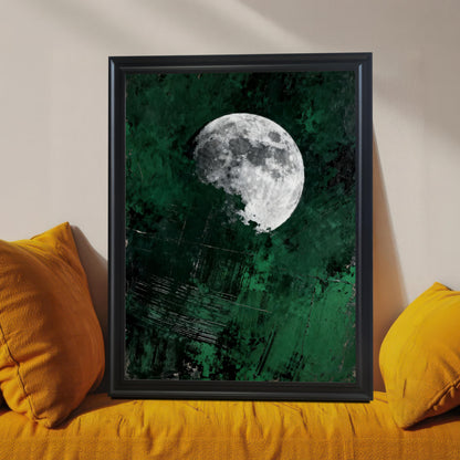 Close-up of a black wood-framed moon art print leaning on a vibrant orange textured sofa, highlighting the detail of the emerald green background and high-contrast moon.