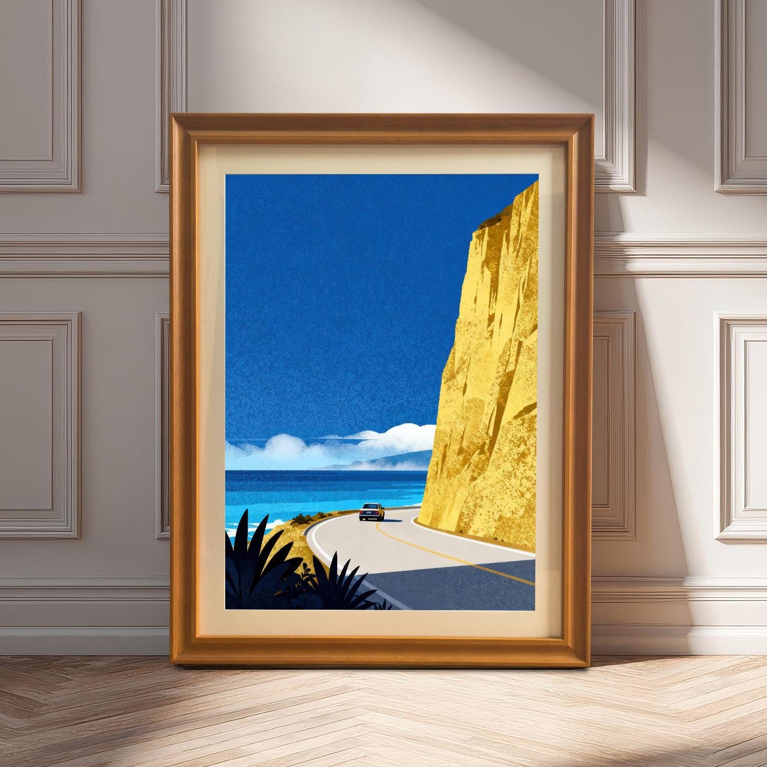 An orange-toned wood-framed art print with a cream mount leaning on a light-colored wooden floor against a classic paneled wall in sunlight.