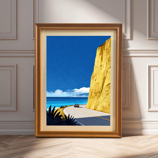 An orange-toned wood-framed art print with a cream mount leaning on a light-colored wooden floor against a classic paneled wall in sunlight.