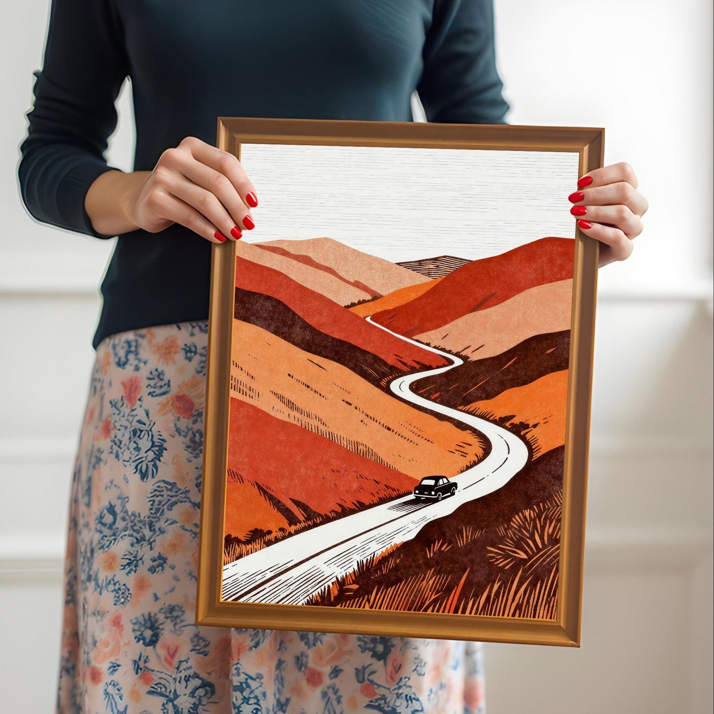 A person holding the orange-framed art print to provide a real-world sense of scale and showing the vibrant colors of the winding road illustration.