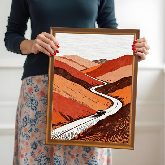 A person holding the orange-framed art print to provide a real-world sense of scale and showing the vibrant colors of the winding road illustration.