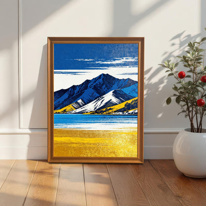 A vertically oriented framed art print featuring a stylized landscape in bright blue and yellow, with snow-capped mountains and a gold-colored foreground, leaning on a wooden floor against a white wainscoting wall next to a potted plant with red berries. The frame is a light brown/orange wood.