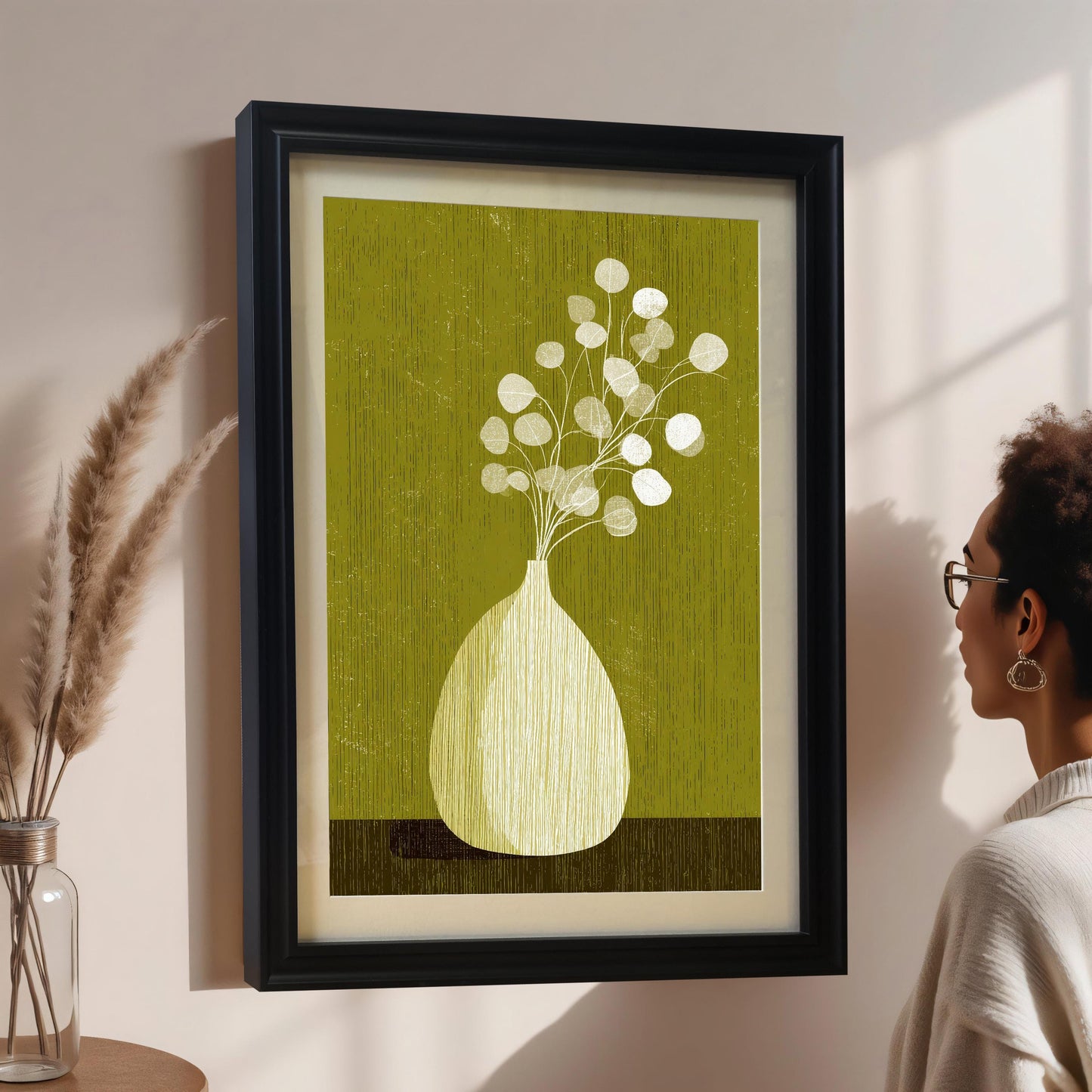 A woman in profile viewing a large botanical art print in a black wood frame with a white mount, hanging on a neutral-toned wall with soft natural lighting.