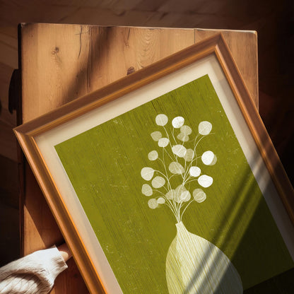 High-angle shot of a framed art print in an orange wood frame with a mount, resting on a rustic wooden table with natural sunlight.