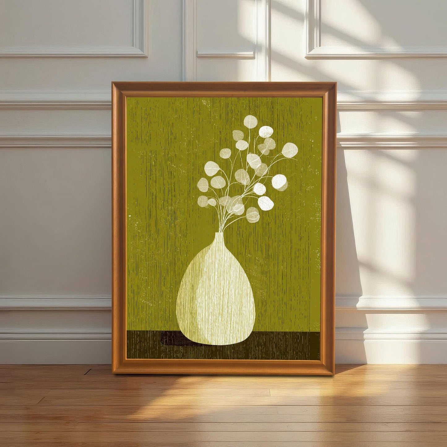 Large-scale olive green botanical art print in an orange wood frame leaning against a white wainscoted wall on a polished hardwood floor with window shadows.