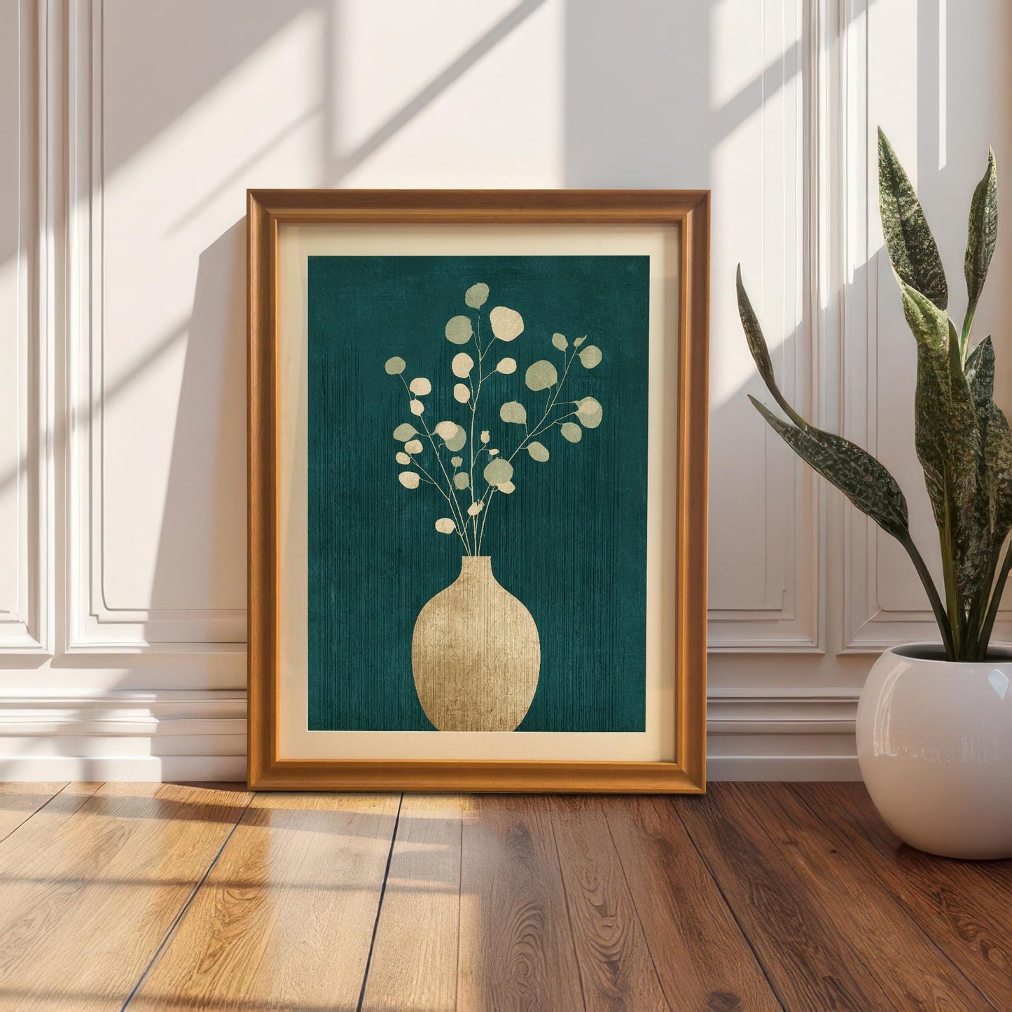 A large orange-framed botanical print with a cream mount leaning against a classic white paneled wall on a hardwood floor next to a potted snake plant.