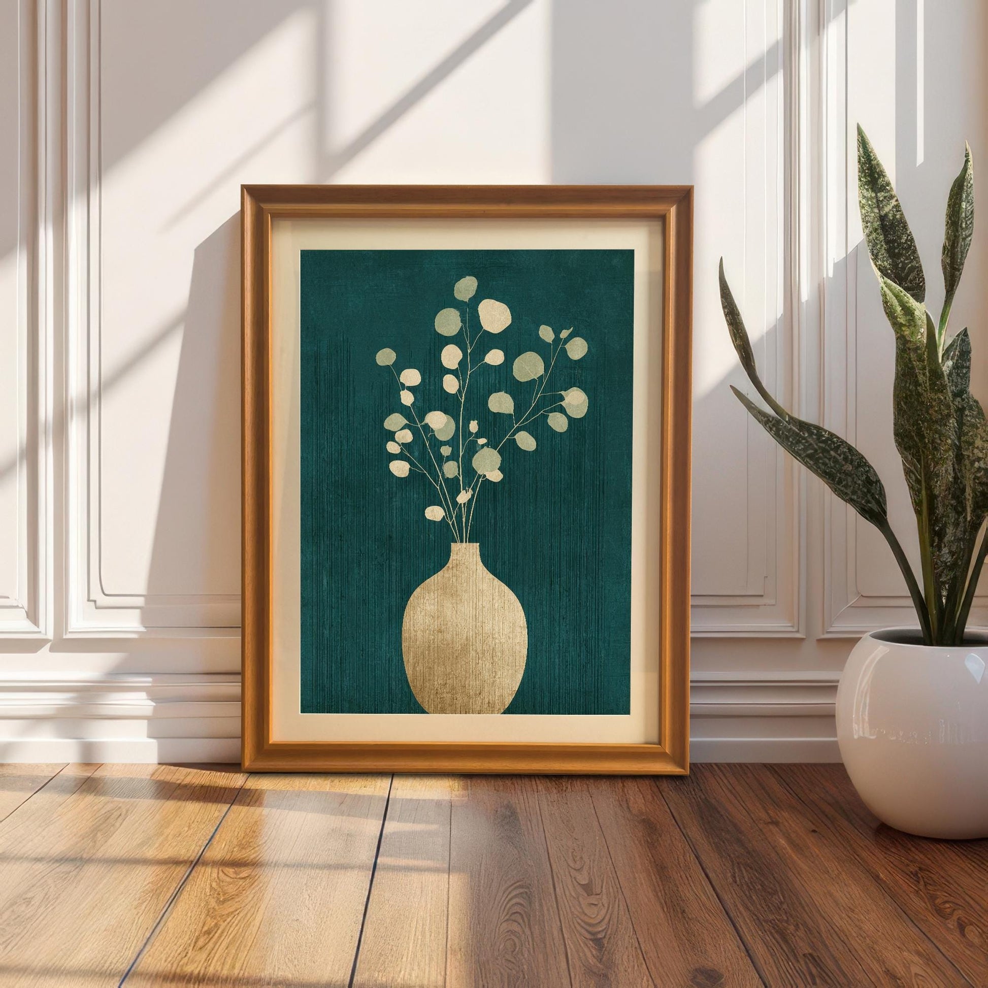 A large orange-framed botanical print with a cream mount leaning against a classic white paneled wall on a hardwood floor next to a potted snake plant.