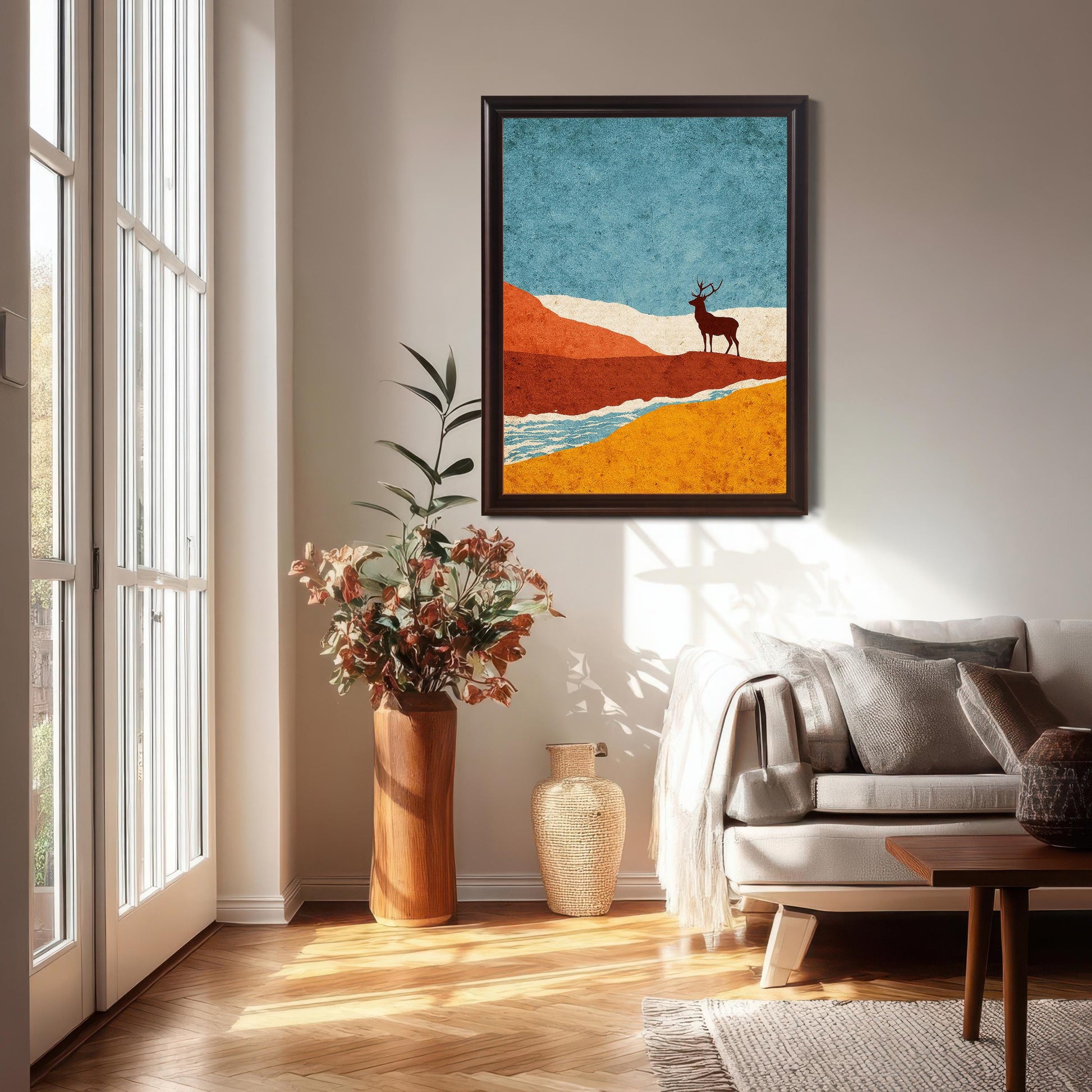 A vertical dark-wood coffee frame featuring the colorful stag landscape hung in a bright, modern living room above a white sofa with neutral pillows and a large floor vase.