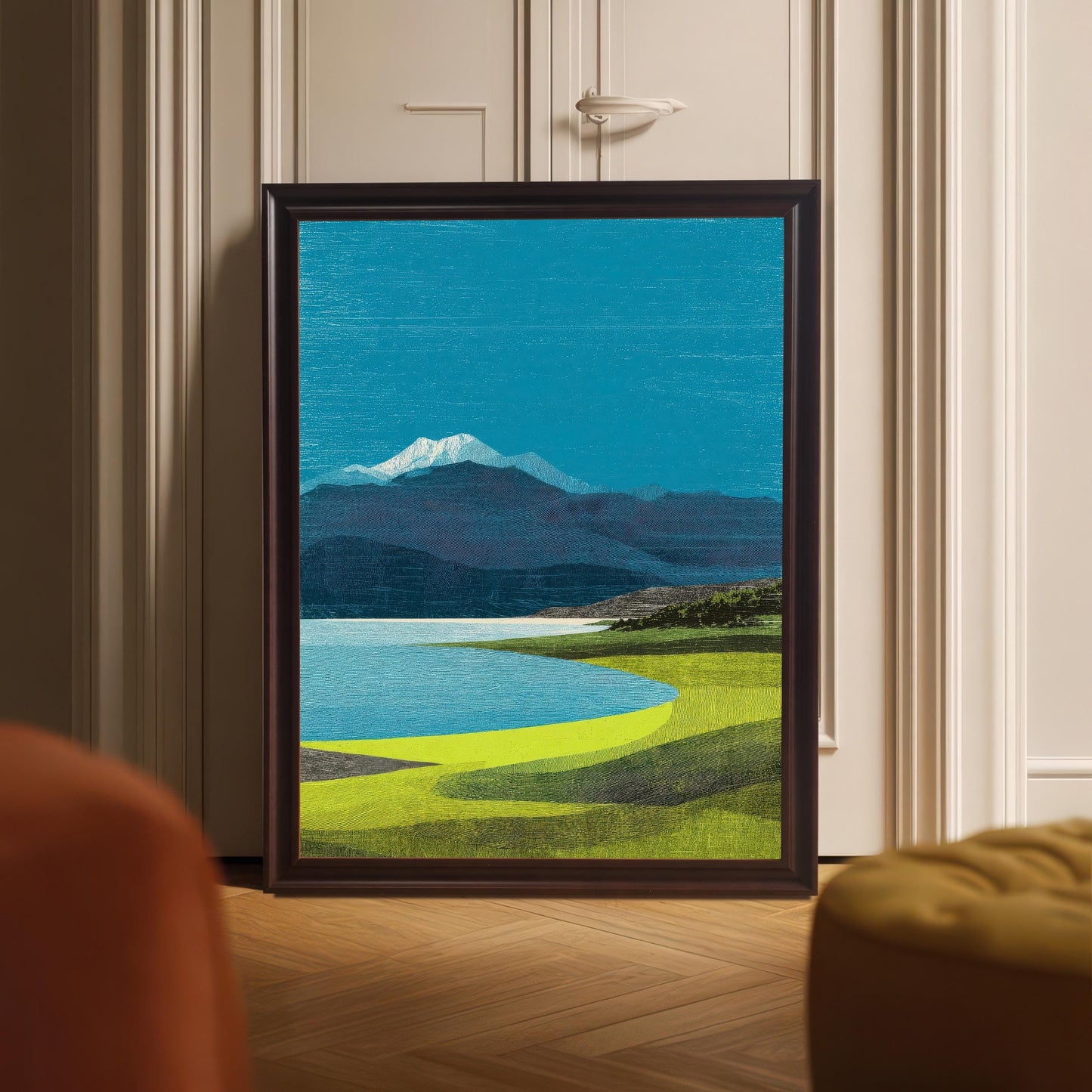 A large dark wood-framed art print of a blue lake and snow-capped mountain leaning against a white paneled door on a herringbone wood floor.